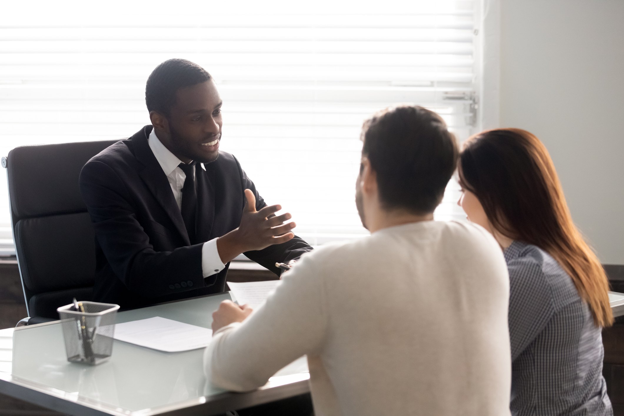 A couple has a discussion with a businessman at a desk.