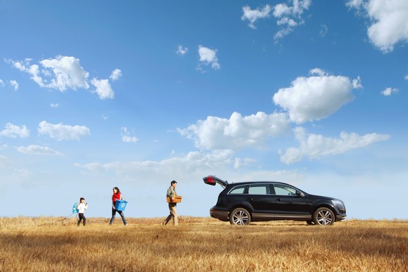 Family in the middle of a wide-open field walking to and from their car on a beautiful day.