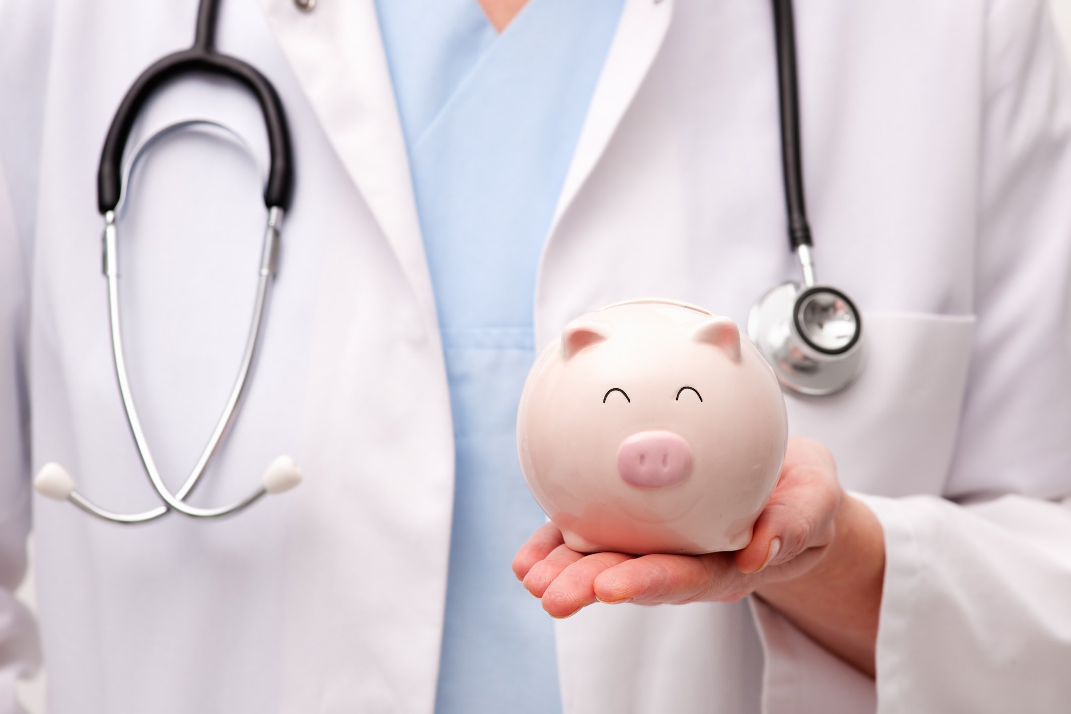 A person in a white coat wearing a stethoscope holding a piggy bank.