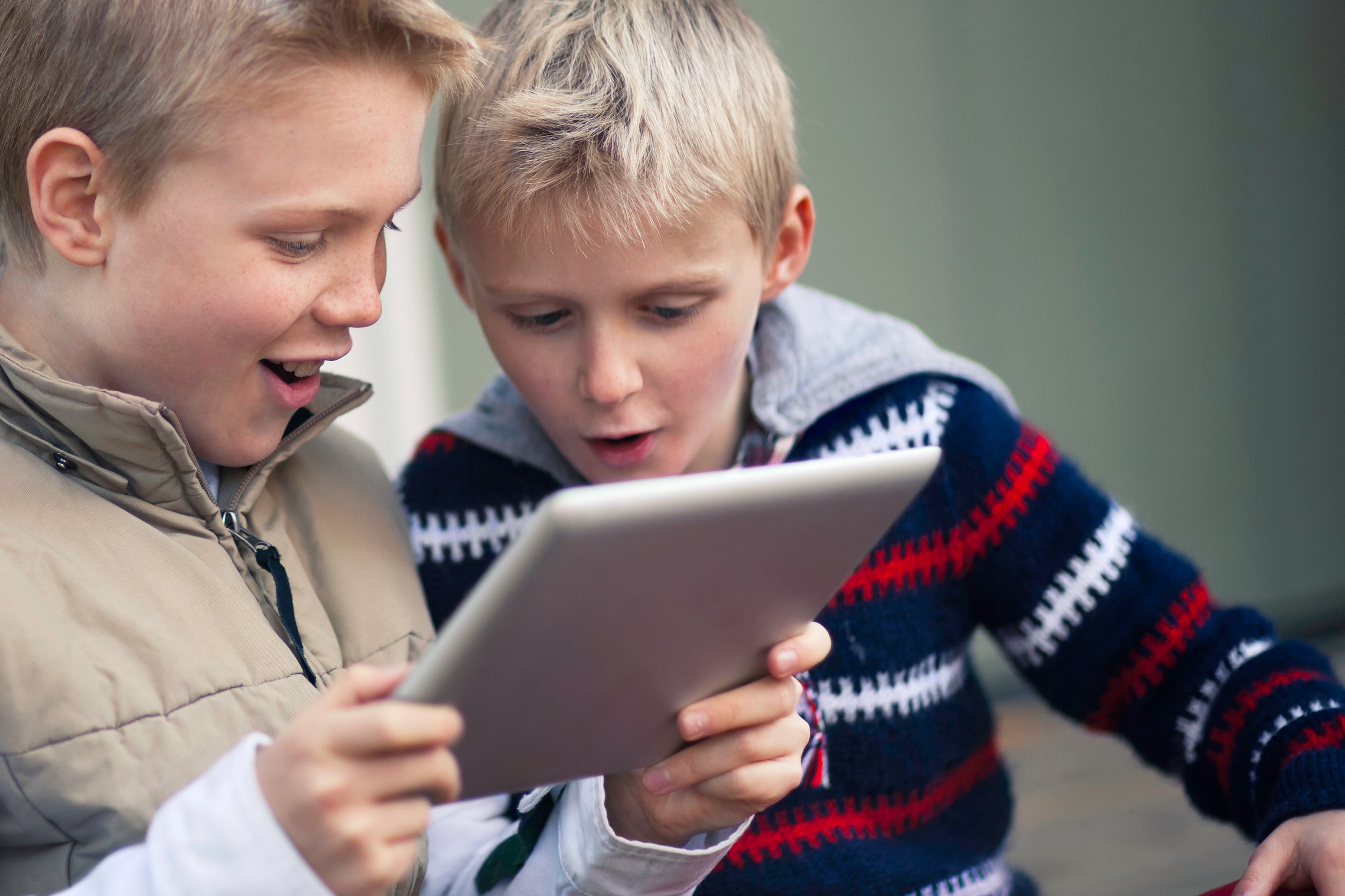 Two kids playing a game on a tablet.