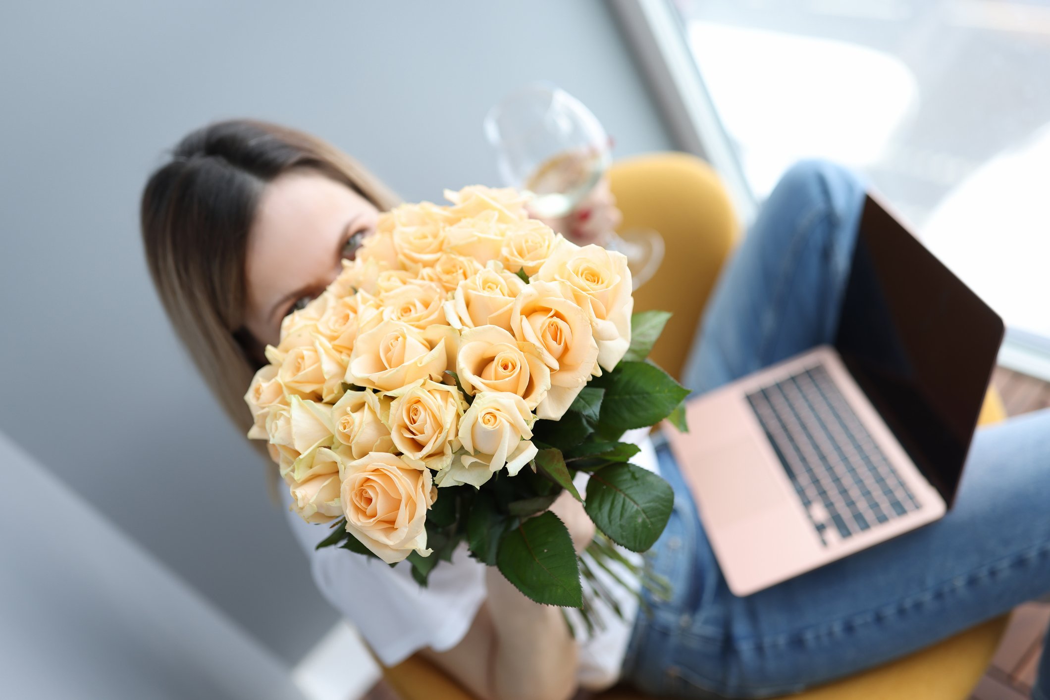 A laptop user holding a large bouquet of cream-colored roses.