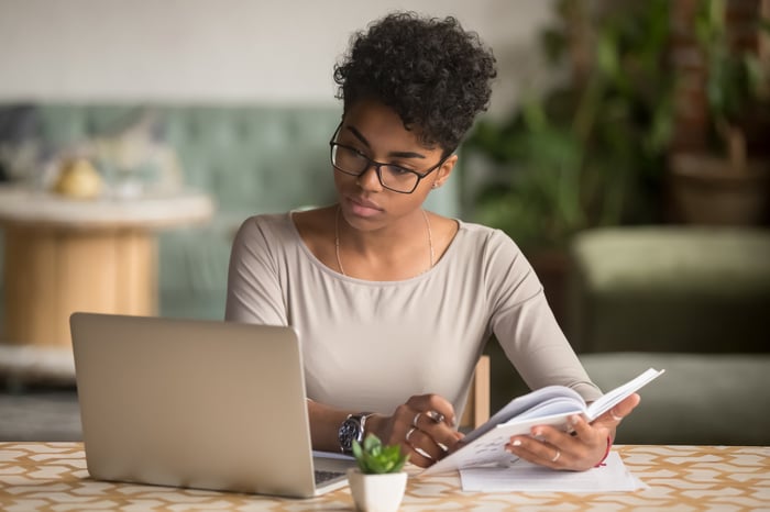 Person looking at a laptop and holding a book