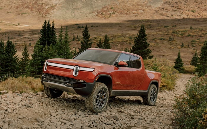 A red Rivian R1T, an upscale electric off-road pickup, on a gravel backroad. 