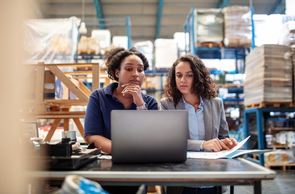 Two people at a laptop in a warehouse.