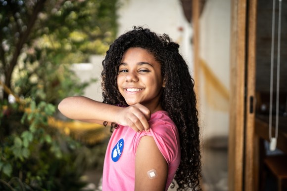 Smiling young person showing off vaccine shot bandage on her arm.