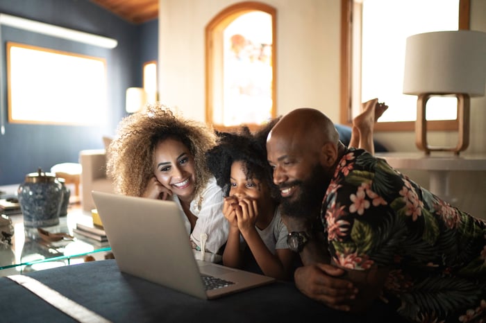 Three people in a living room looking into a laptop screen.