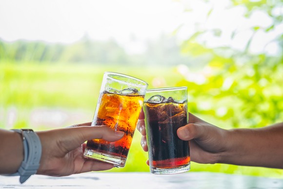 Two people clinking glasses filled with soda.
