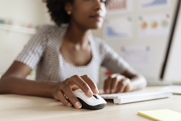 A remote worker holding a computer mouse on a desk.