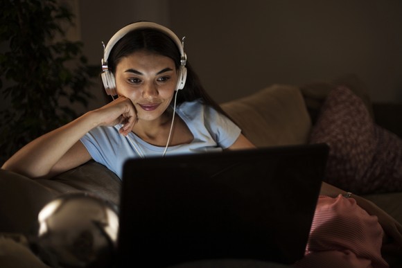 Woman wearing headphones while watching content on her computer.