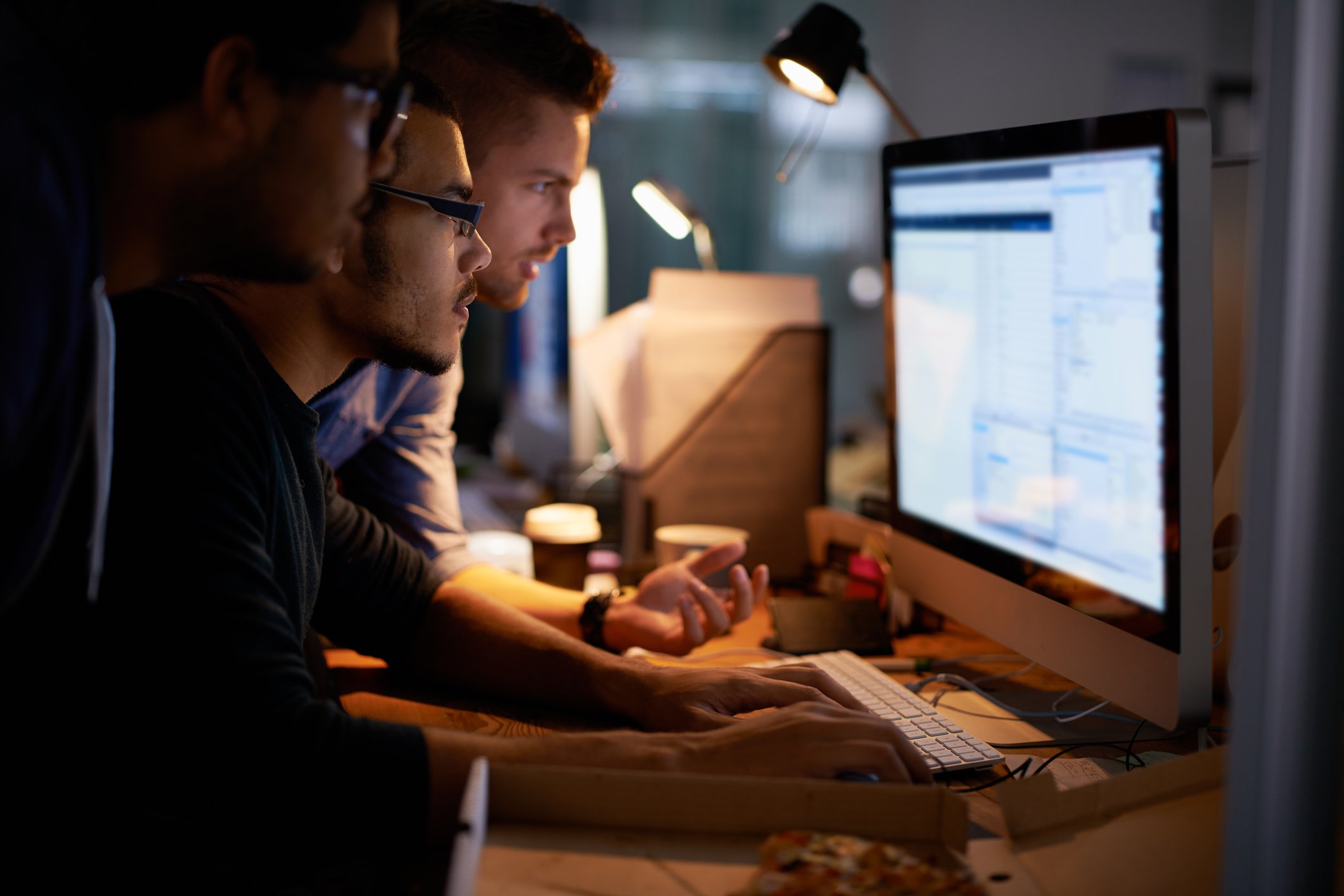 Three people hunched over a screen looking at data. 