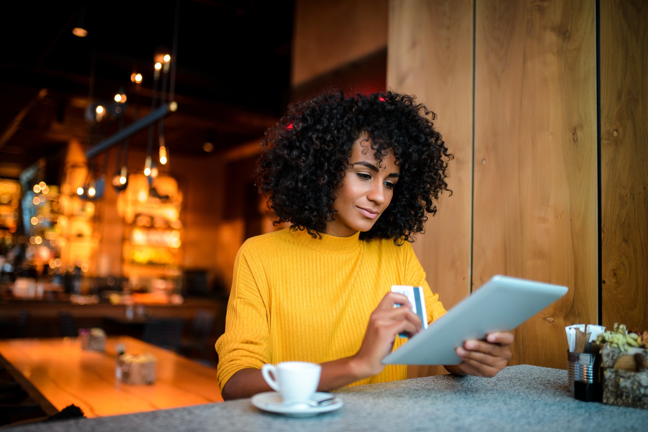 Person holding tablet and credit card at a cafe.