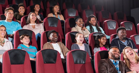 Smiling people watch a movie in a theater.