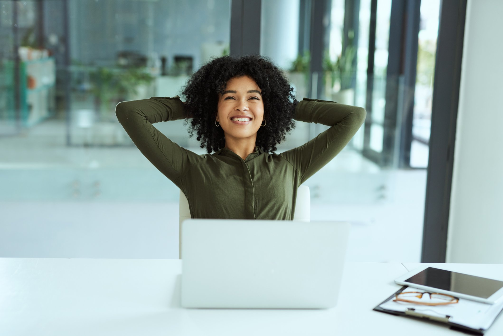 A smiling person with hands behind head sitting in front of a laptop.