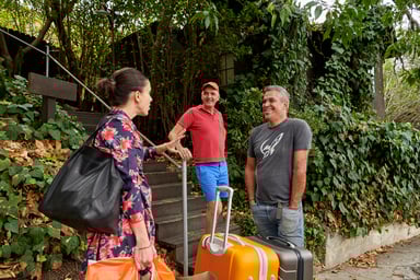 Three people standing in a garden with suitcases