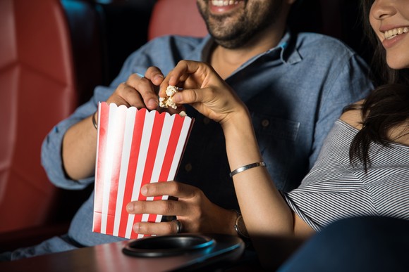 Two people share popcorn while watching a movie.
