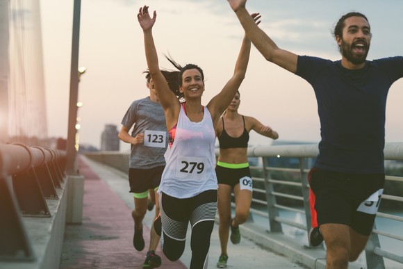 Marathon runners raising their hands as they cross a bridge.