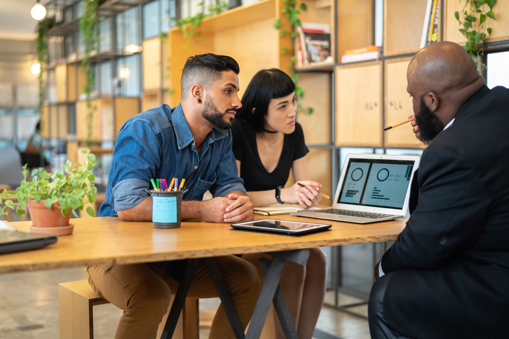 Three people consider charts on a shared laptop screen.