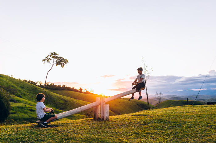 Two children on a seesaw in a field near sunset.