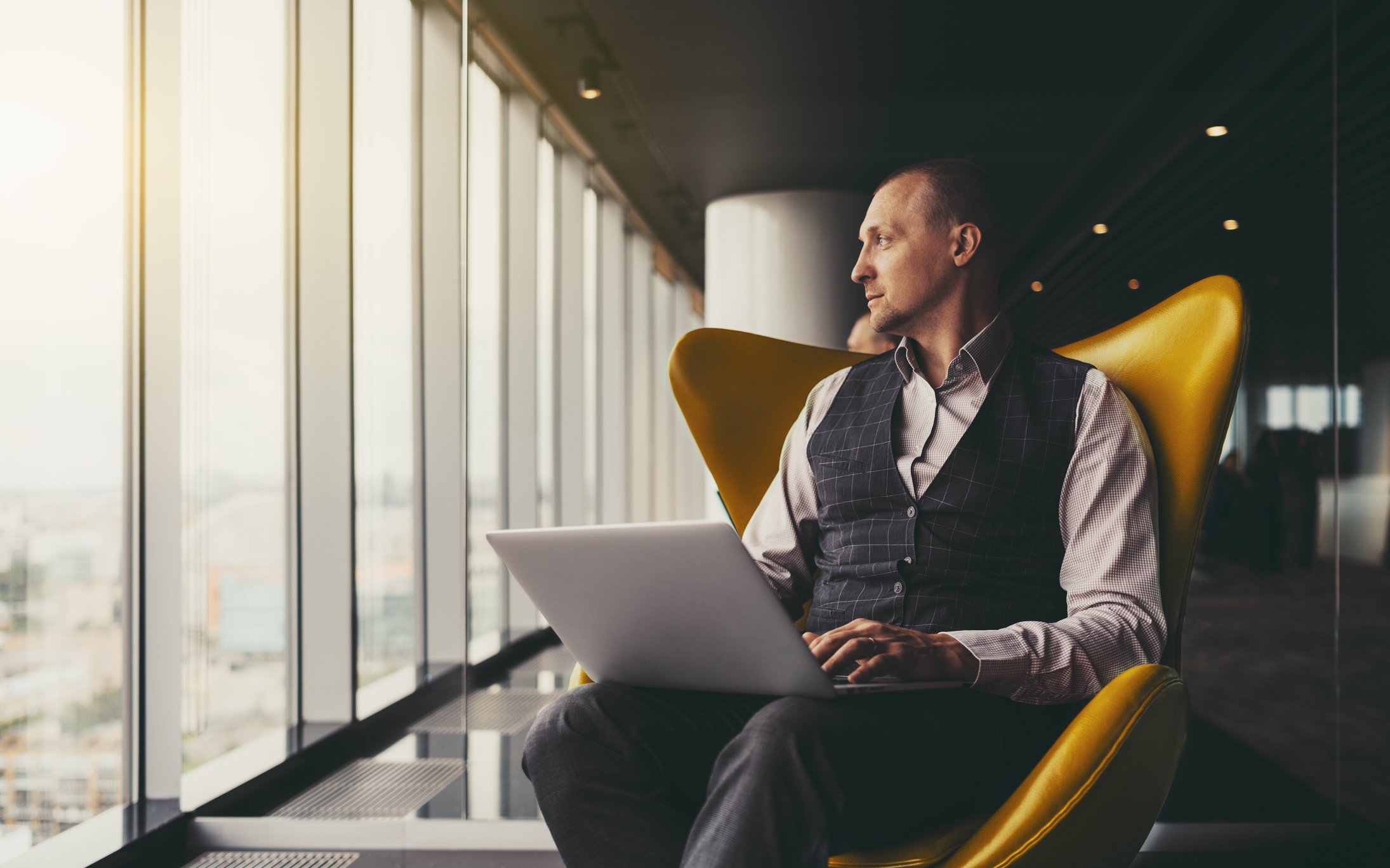A person sitting beside a window, using a laptop.