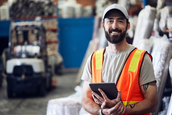 Person smiling wearing vest inside of an industrial warehouse.