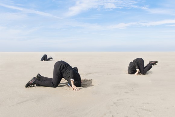 Three businessmen sticking their heads in the sand. 