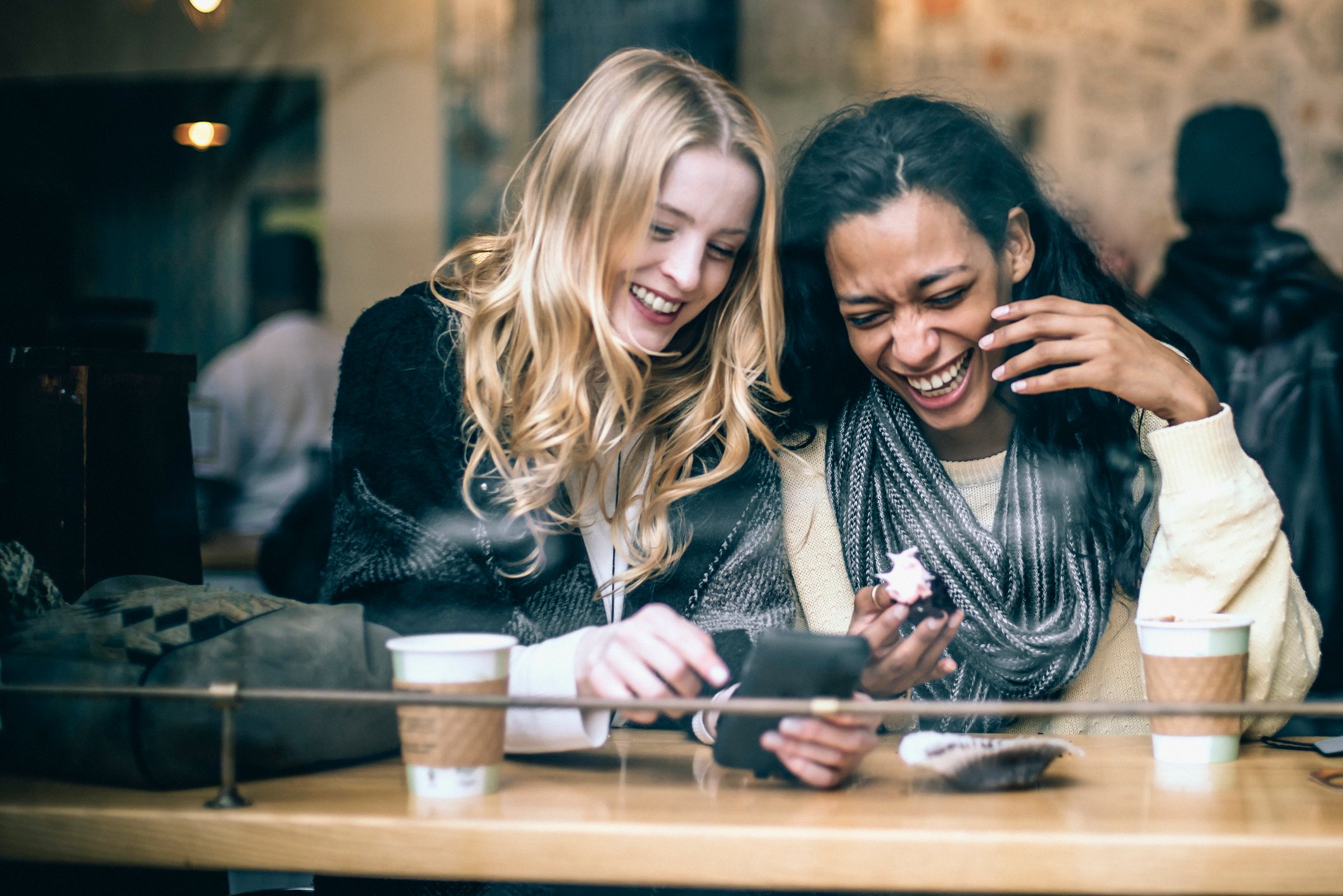 Two people looking at a phone and drinking coffee in a coffee shop.