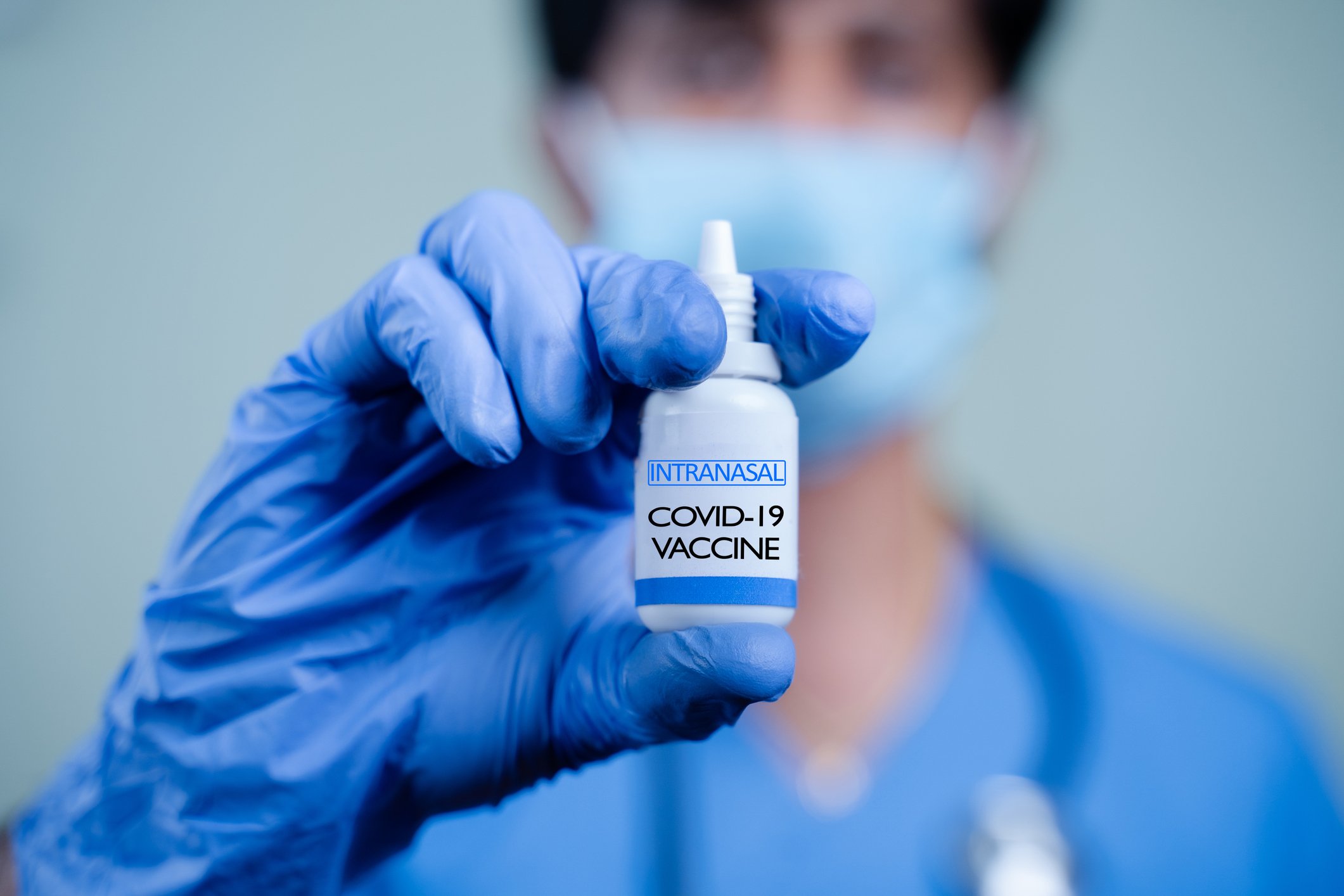 A nurse holds up a vial of an intranasal coronavirus vaccine while clad in protective gear.