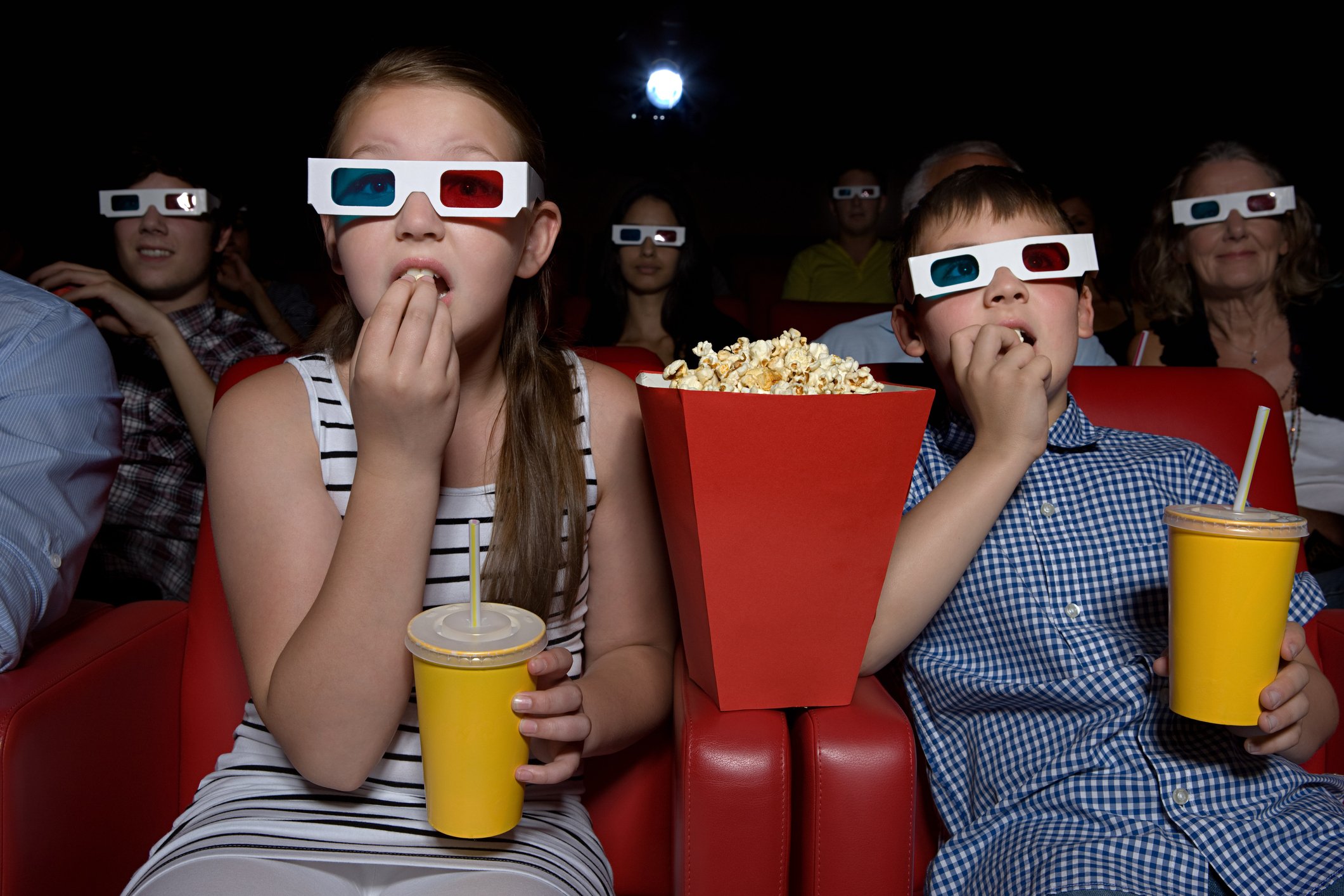 A group of people eating popcorn and watching a movie in a movie theater.