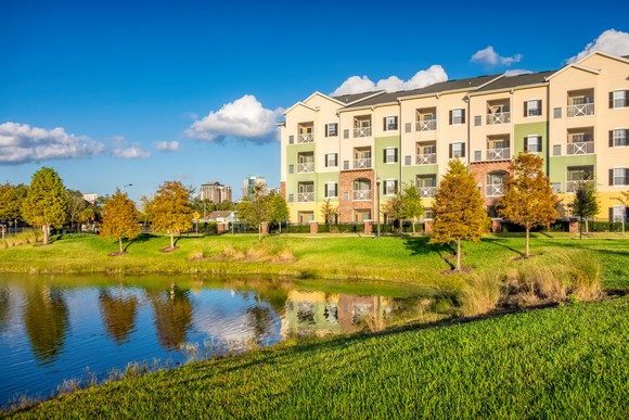 Apartment complex overlooking a small lake with trees.