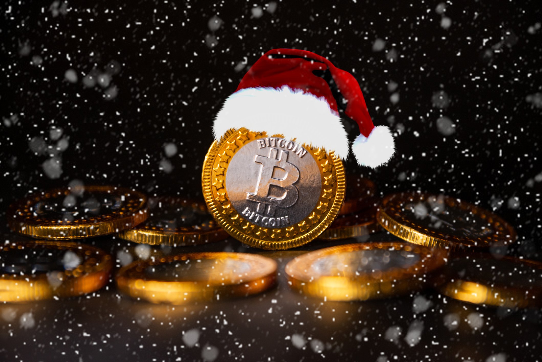 A gold coin with the Bitcoin logo wearing a Santa cap in the snow.