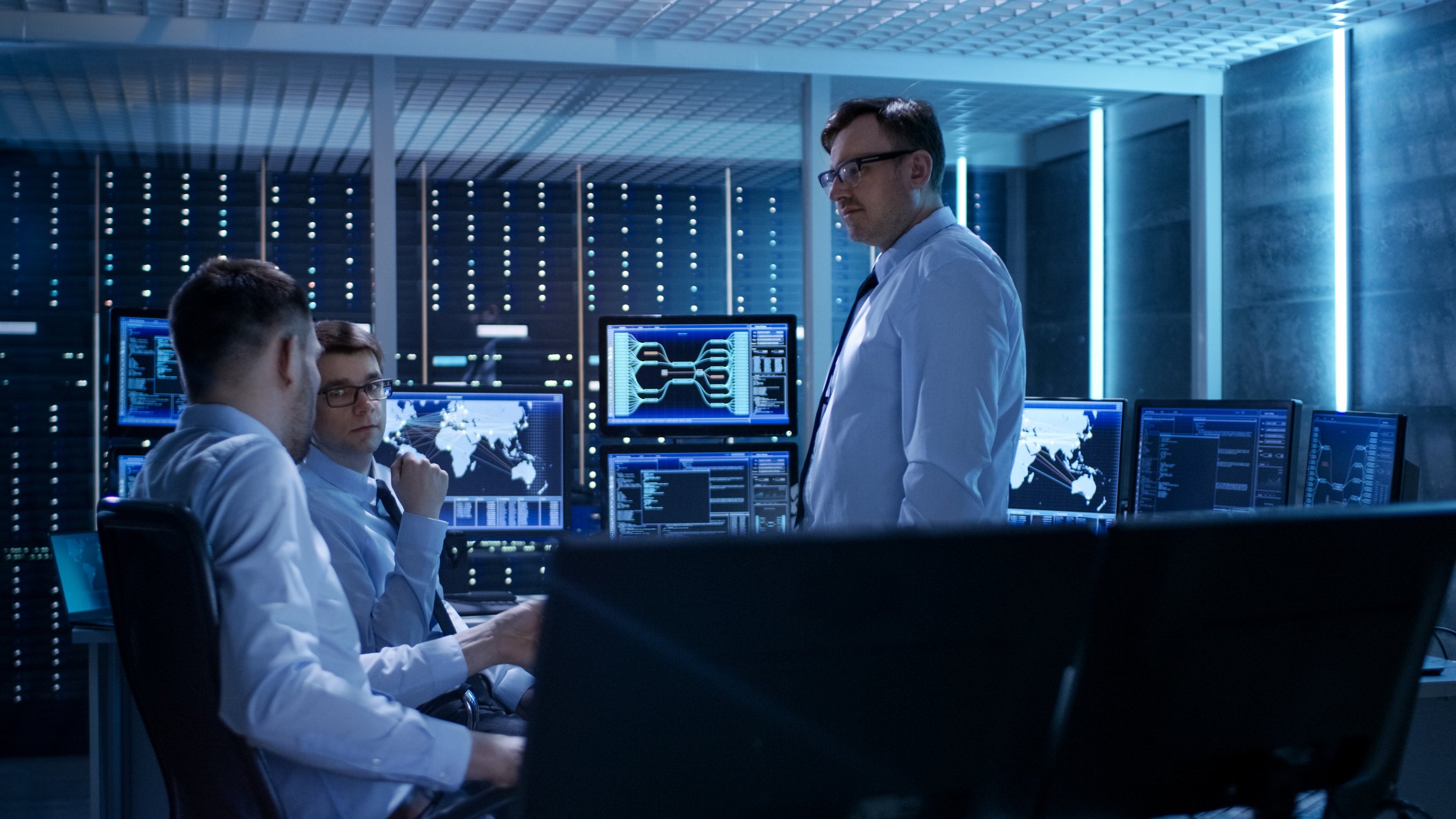 Three people engaged in discussions in a data center control room.