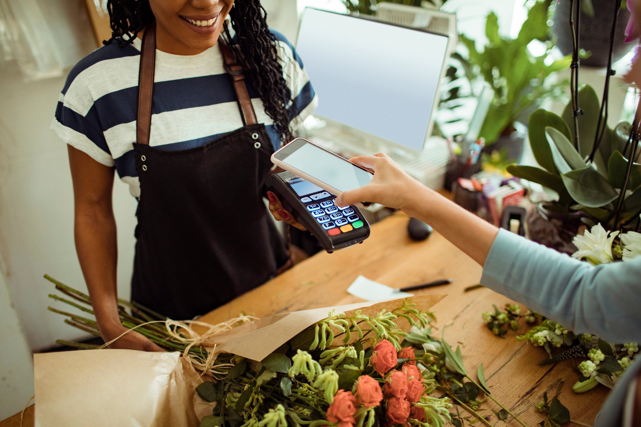 A person in a flower store paying with a mobile phone.