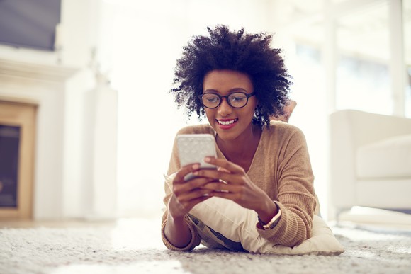 A person uses a smartphone while stretched out on a living room floor. 