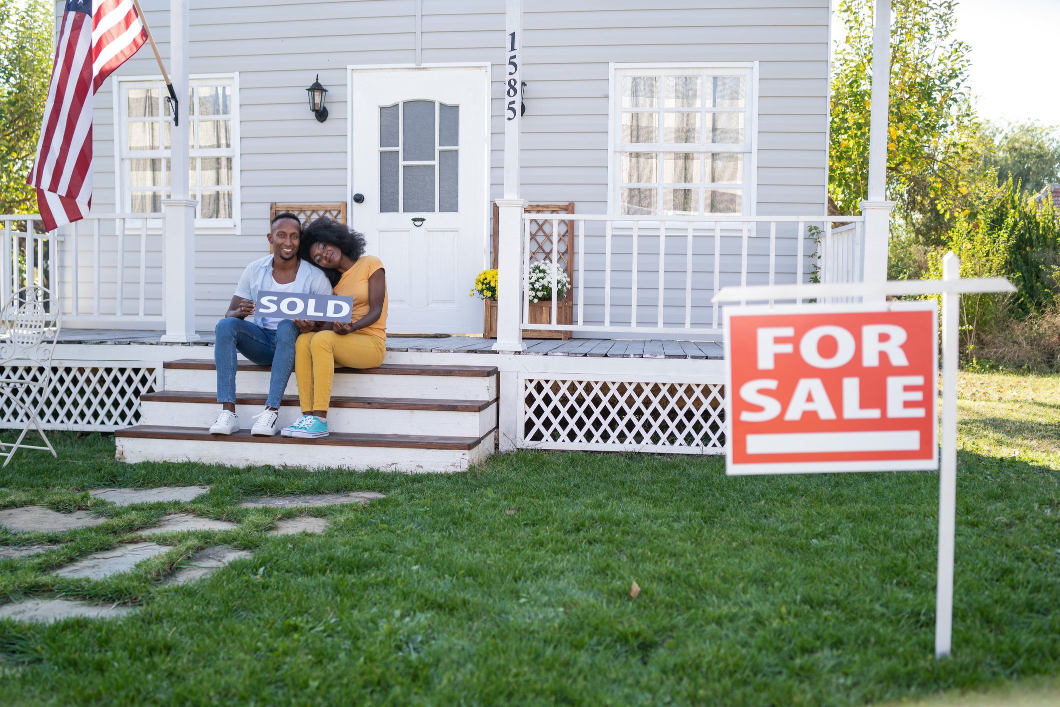 Couple sitting on couch holding a "sold" sign.