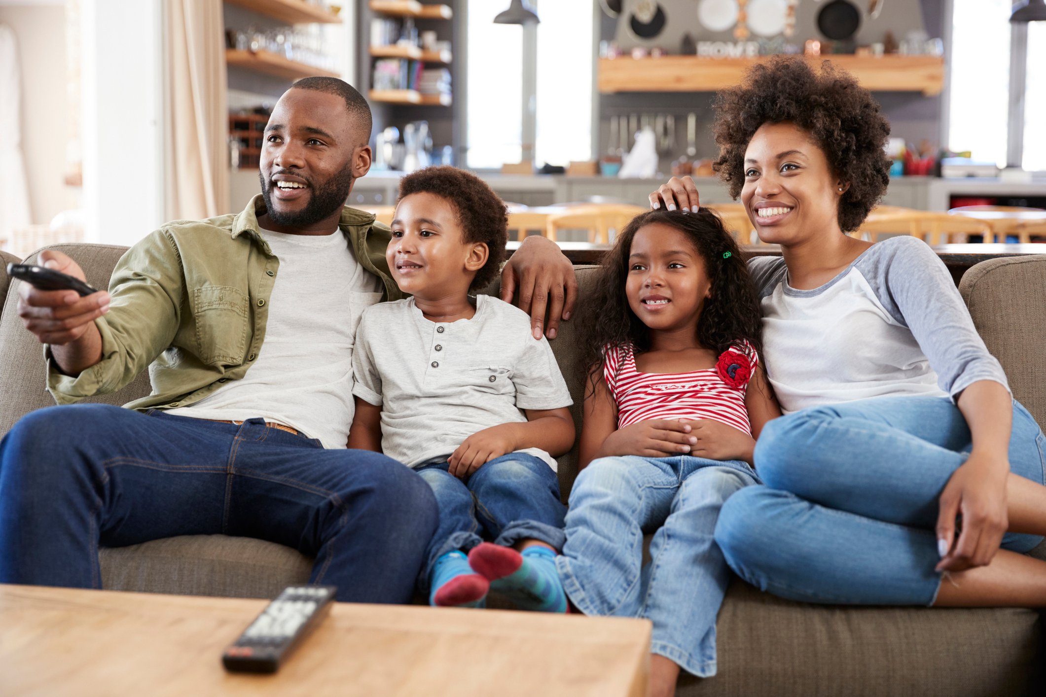 Two parents and two kids on a couch watching TV.