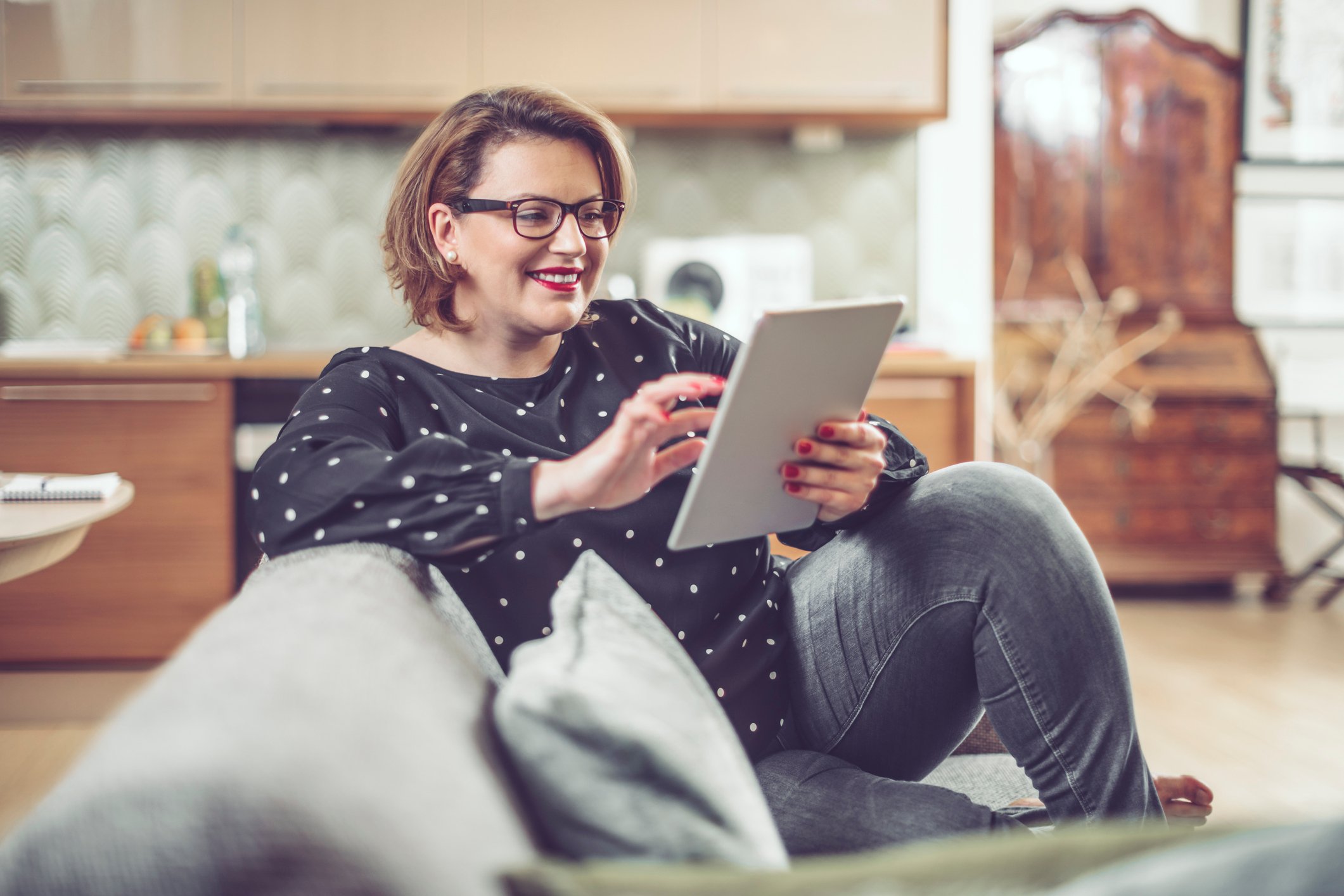 A person on couch, looking at finances on tablet, smiling. 