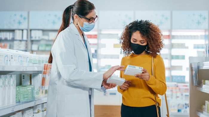 A person in a lab coat showing a product to a customer in a drugstore.