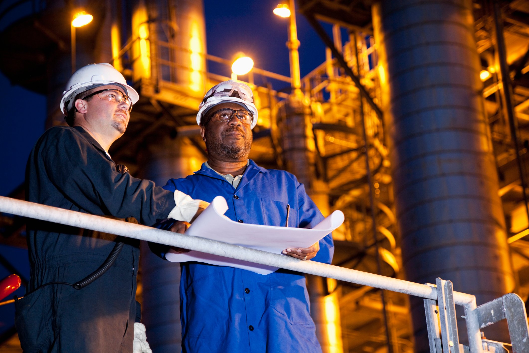 Two workers reviewing plans at an oil refinery