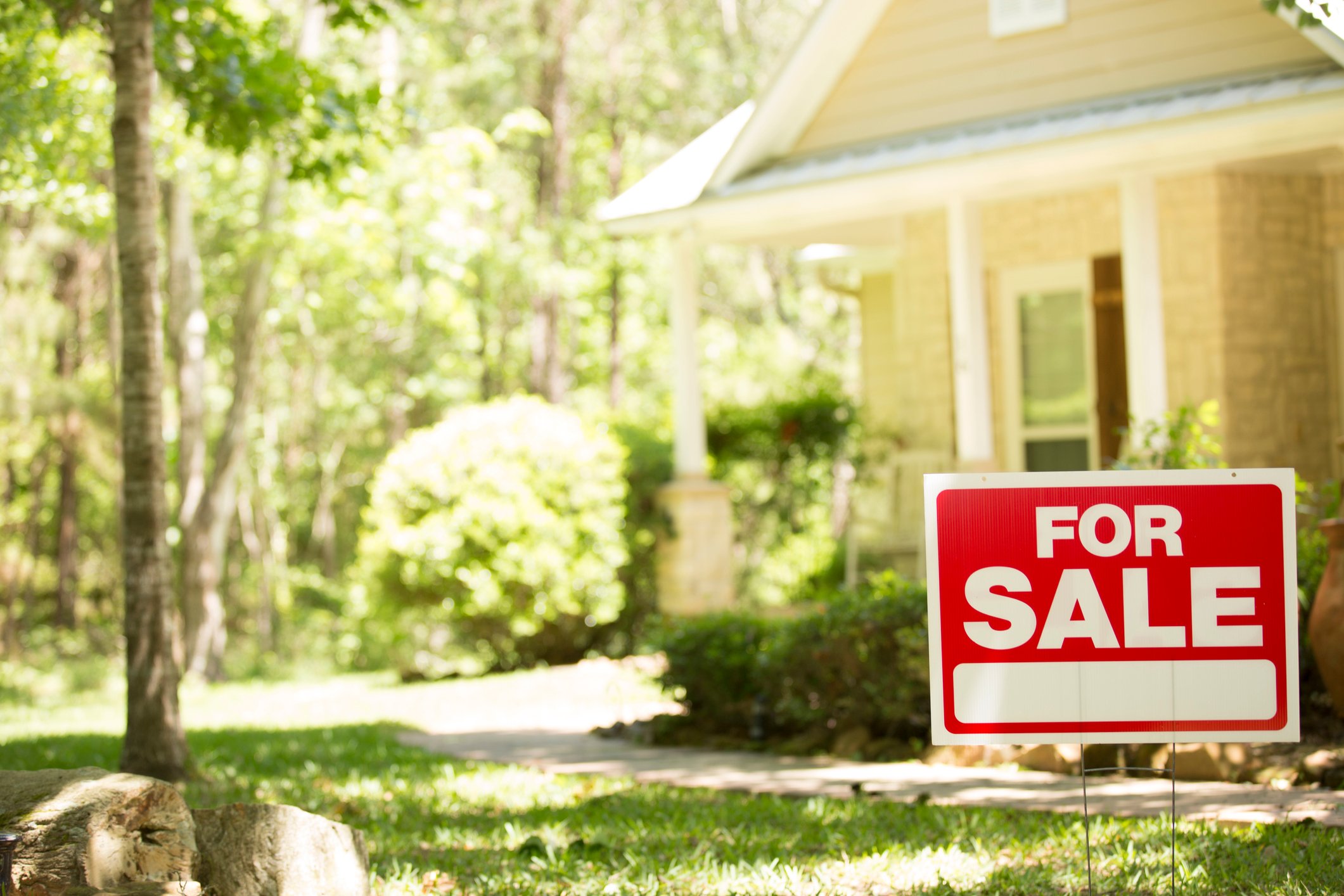 A home on a spring day with a for sale sign in green grass.