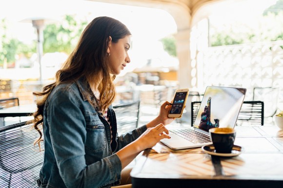 Person holding phone while sitting at table with computer open.