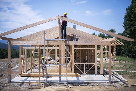 Two people working on the frame of a stick-built house.
