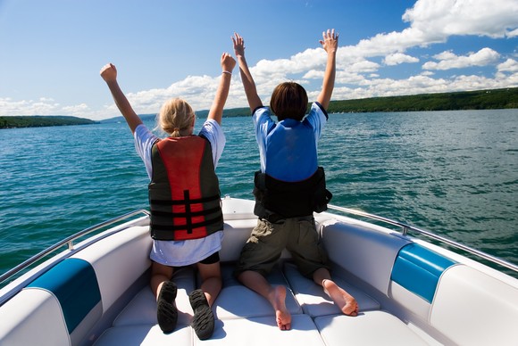Two youngsters kneeling in the bow of a boat with arms raised.