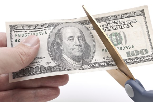 $100 bill being cut by a pair of scissors.