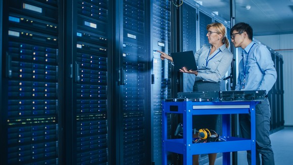 Two people with an equipment cart working on a data center stack.
