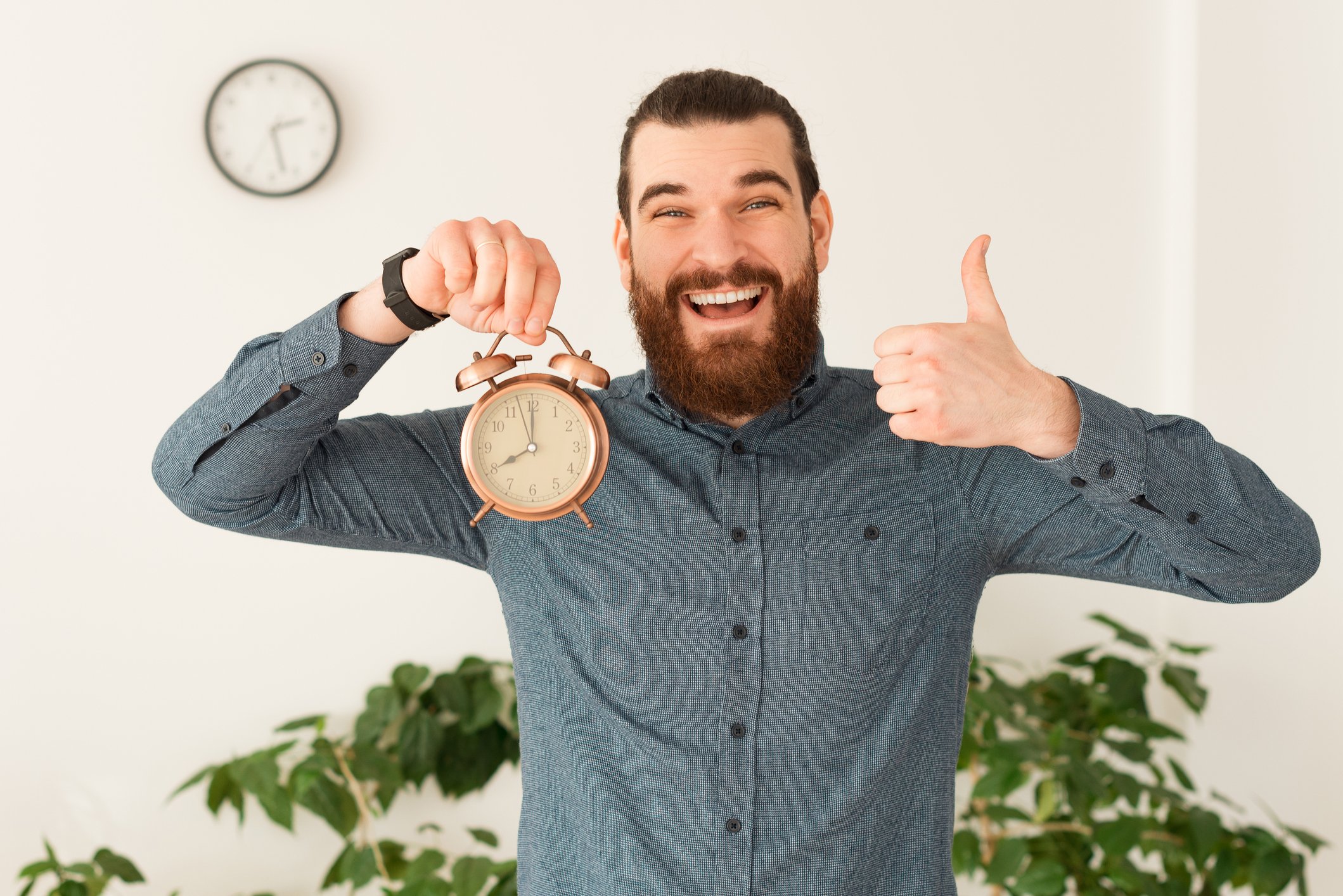 Person smiling and holding a clock in one hand and giving a thumbs-up with the other.