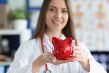 medical worker smiles holding red piggy bank