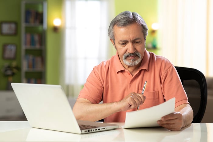 Mature person holding pen and looking at document.