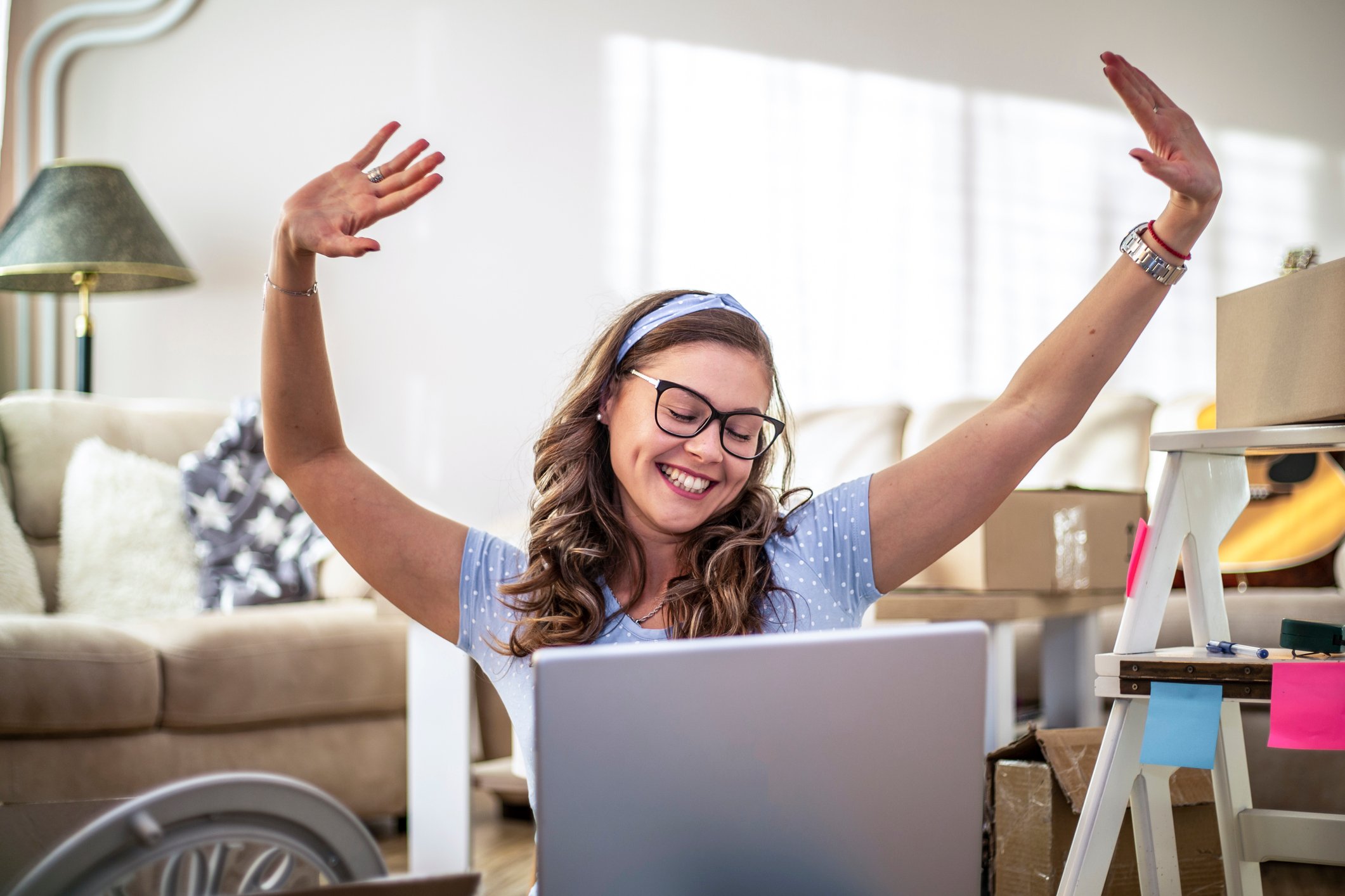 Woman sitting in front of laptop smiling and raising arms in celebration.