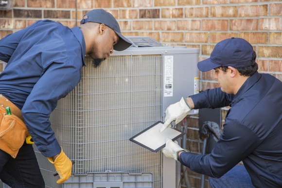 Two repairmen work on an air conditioning unit.