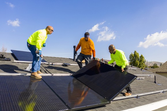 A team of workers installs solar panels onto a residential building. 